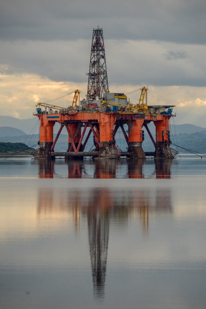A large offshore oil rig reflects in calm waters under a cloudy sky, United Kingdom.